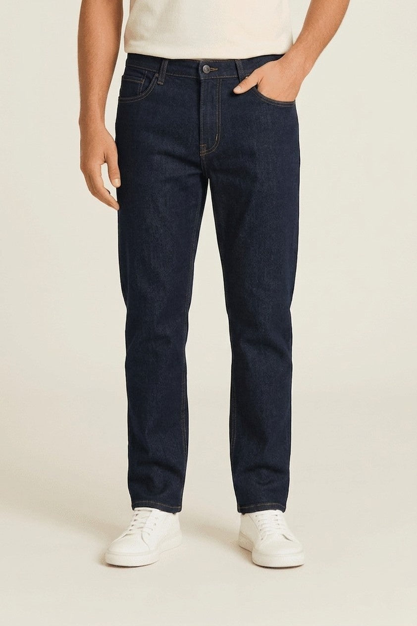 Person wearing dark blue jeans and white sneakers on a plain background