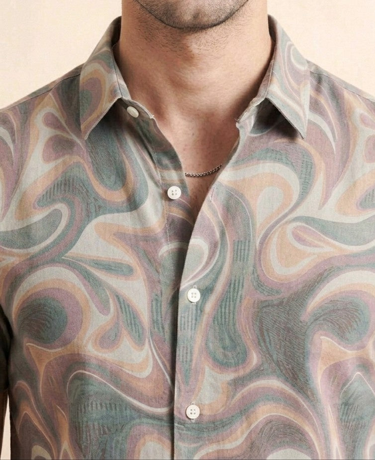 Man wearing a patterned shirt with his arms crossed on a beige background